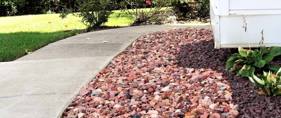 Rock mulch installed in a landscaping bed beside a sidewalk at a residential property.